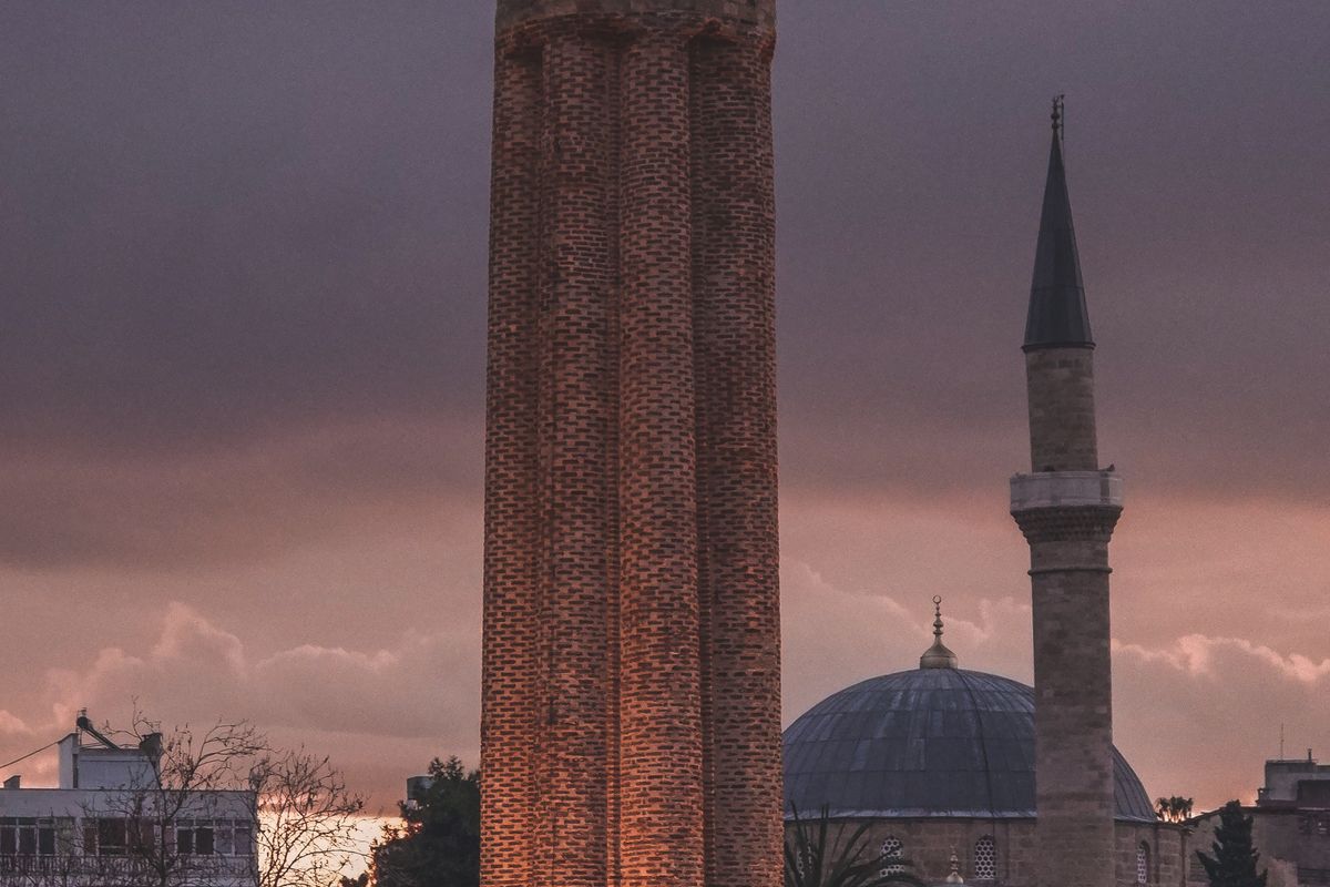 The fluted red-brick Yivli minaret of Antalya at dusk beside a domed mosque