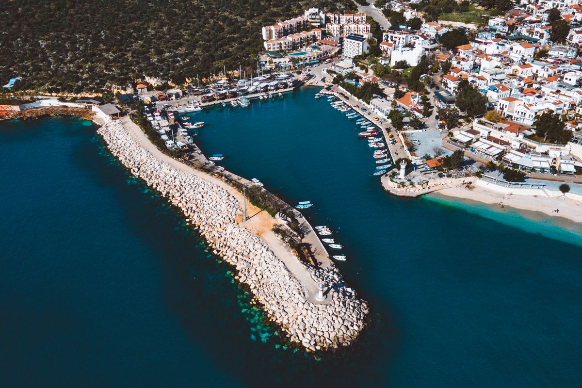 Aerial view of Kalkan's curved stone harbour breakwater, marina boats and the white town climbing the hillside